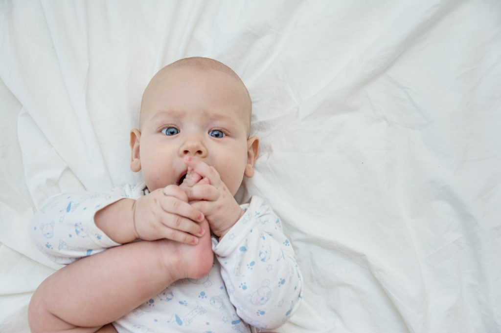 Półroczne dziecko próbuje zjeść palca u nogi